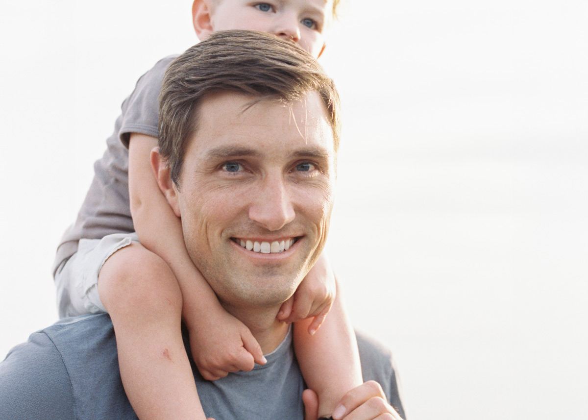 Padre sonriendo sosteniendo a su hijo en los hombros