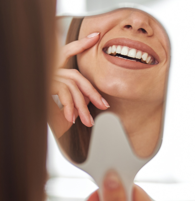 Mujer mirando en un espejo de mano su sonrisa blanca y alineada.