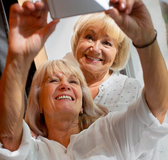 Dos mujeres maduras sonriendo y haciéndose un selfie.