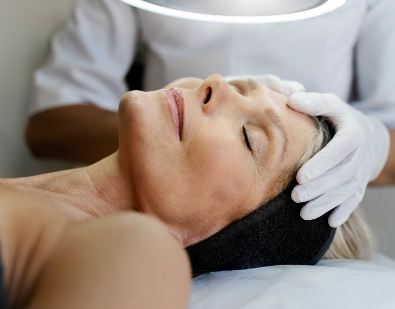 Mujer madura estirada en una camilla recibiendo un tratamiento facial