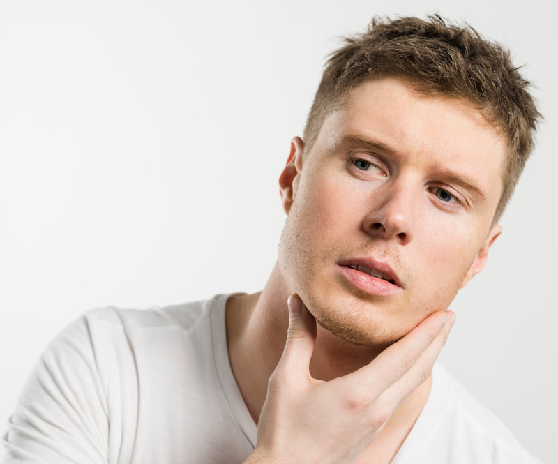 Chico joven con la mano en su barbilla ligeramente inclinado.
