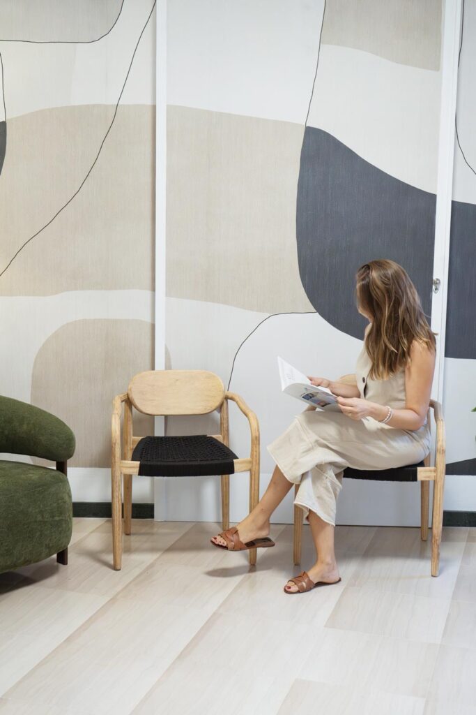 Chica de espaldas leyendo sentada en una silla de madera de una sala de espera moderna y elegante