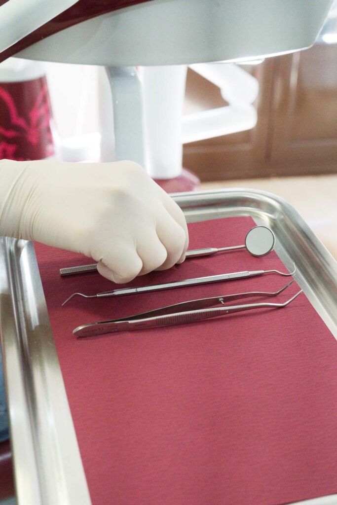 Bandeja con instrumental de dentista, una mano con guante de látex está cogiendo uno de los instrumentos