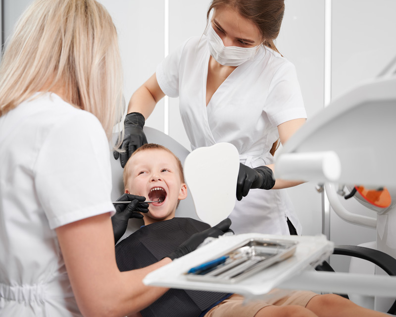 Niño sonriente sentado en la butaca del dentista mientras le miran la boca