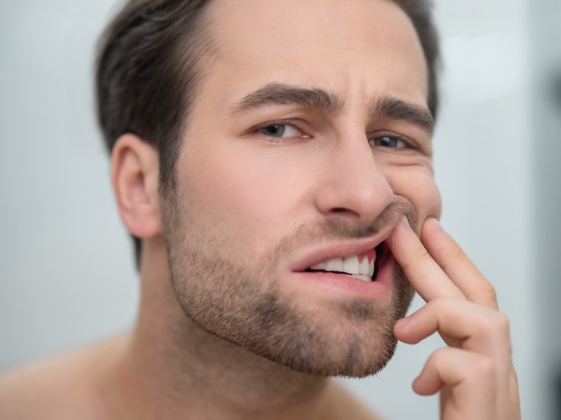 Hombre joven mirándose las encías con expresión de dolor.