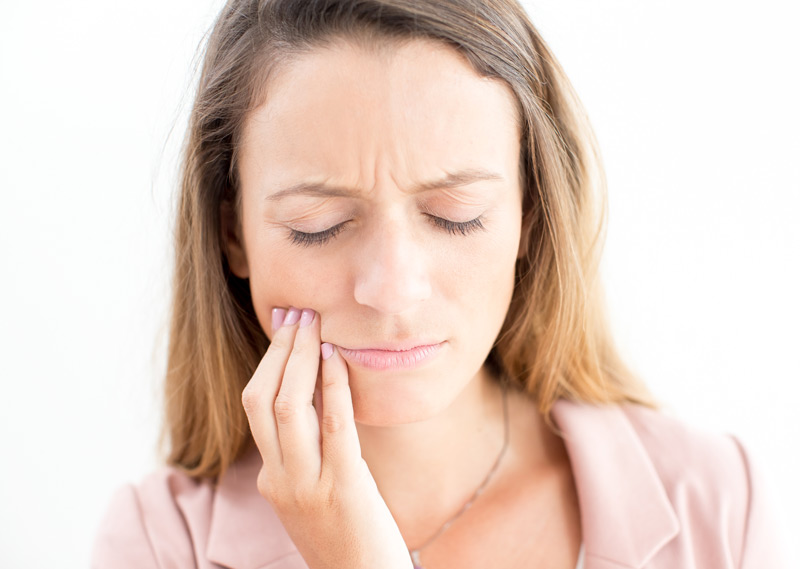 Chica con los ojos cerrados, expresión de dolor y con una mano se toca con cierta intensidad una de las mejillas.